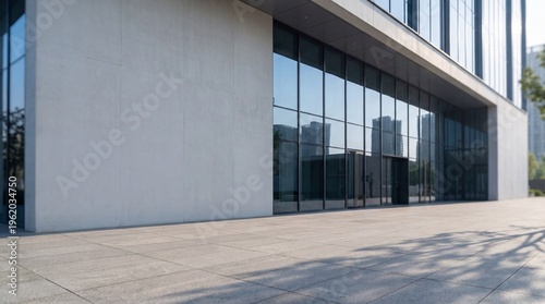 Modern office building exterior with large glass windows and minimalist design. Wide entrance, tiled pavement, and reflections of cityscape create clean, bright urban architecture scene