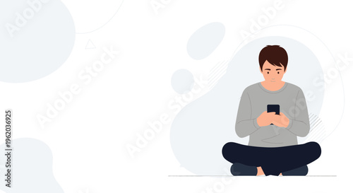 Young man sitting cross-legged on floor, looking at smartphone, minimalist background