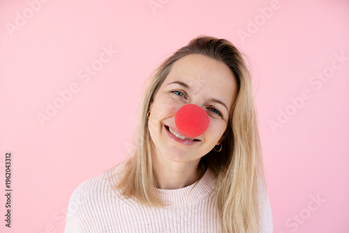blond woman in front of pink background with red clown nose