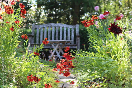 Fényképezés Seat and table in a garden surrounded by flower beds full of heleniums and dahli
