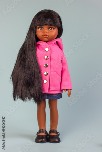 Realistic vinyl toy doll with beautiful dark hair and dark skin in stylish clothes on a blue background, close-up portrait , banner copy space for text