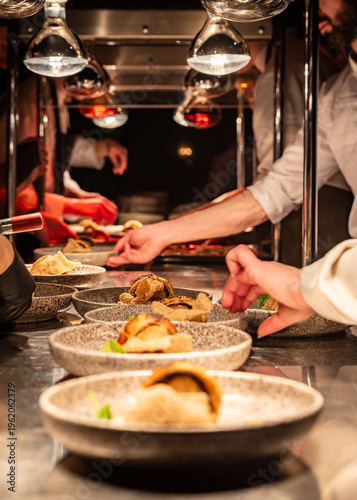 A busy kitchen service area with lots of chefs hands and dishes being prepared for serving to guests
