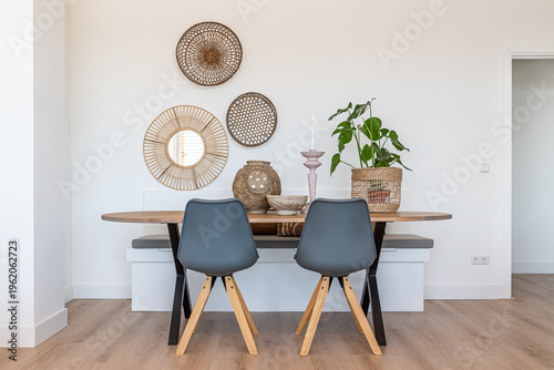 A wooden dining room table with two grey chairs, a plant and various beach themed wall and table decorations in a home lounge with a white wall.