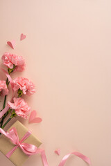 Happy Mother's Day vertical greeting composition featuring pink carnations, a wrapped gift, satin ribbon and paper hearts on a soft pastel background ideal for cards and social posts