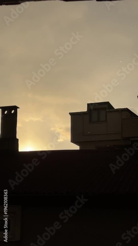 Dark silhouette of apartment building roof against golden stormy sky with snow