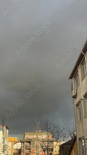Snow appearing over city buildings during a sun shower with dark storm clouds
