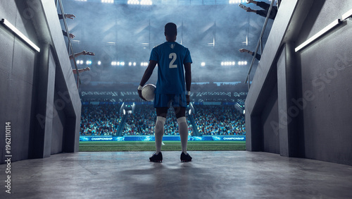Fotografie Black Male Soccer Player Stands at the Tunnel Entrance Holding the Ball, Facing a Packed Stadium Before Kickoff in a Professional International Football Euro and World Tournament Scene