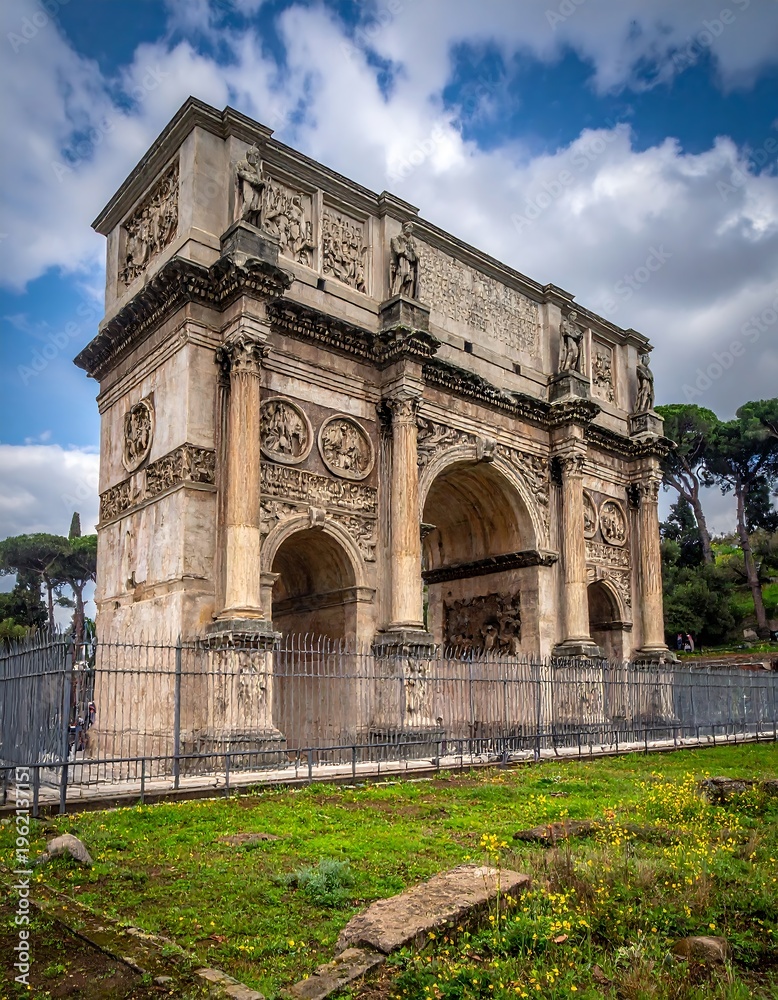 Obraz premium A grand ancient stone archway stands under a cloudy sky. Trees and grass surround it