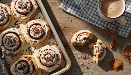 Top view of golden brown cinnamon buns with sweet icing in a baking pan. Comfort food concept with warm cinnamon buns and aromatic coffee in rustic style