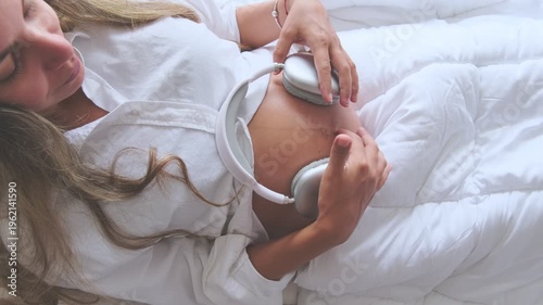 Expectant mother holding headphones on her pregnant belly for her unborn baby to listen to music