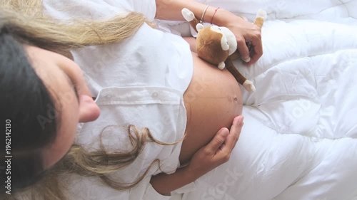 Expectant mother sitting in bed with baby shoes, getting ready for the new arrival
