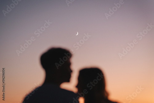 Konstfotografi Blurred silhouettes of a couple against a sunset sky with crescent moo