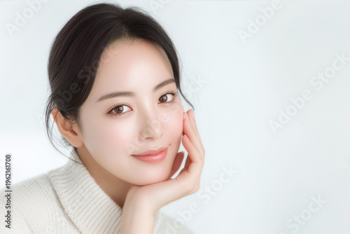 やわらかな光の白い背景で頬に手を添えて微笑む若い女性のナチュラルビューティーポートレート