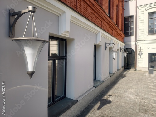 Modern wall-mounted street lamps on a minimalist building facade with geometric lines.