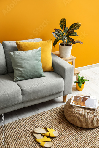Stylish grey sofa and soft pouf near orange wall in living room