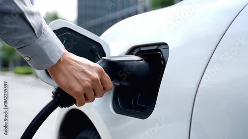 Electric car, close-up person charging white vehicle with modern charger, urban background, symbolizing sustainable energy.