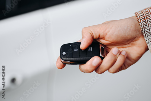 black keys in woman hand, close-up view, white car in background, opening or closing with signalization or alarm system, car theft, carjacking, car safety concept, selective focus