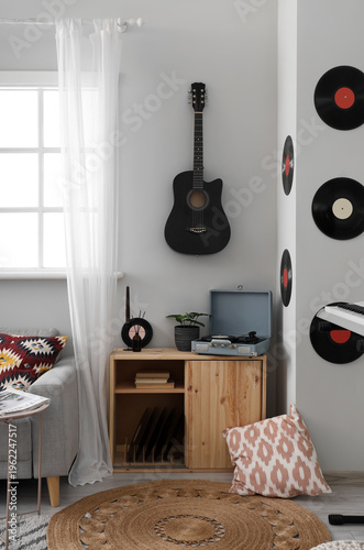 Guitar with vinyl disks hanging on light wall in living room interior