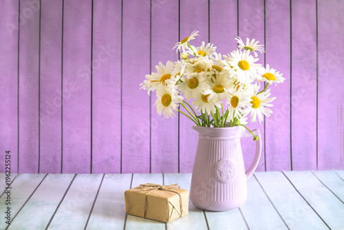 Happy birthday or mothers day greeting card template; bouquet of white daisy flowers and craft gift box on a wooden background; copy space