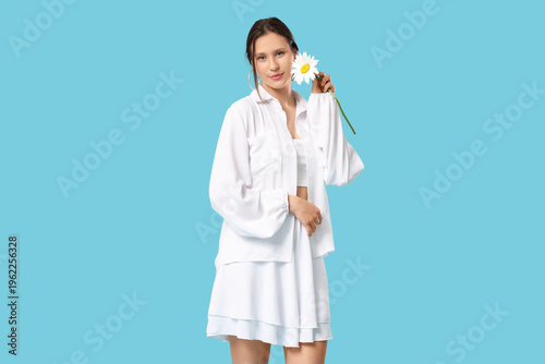 Young woman with chamomile flower on blue background