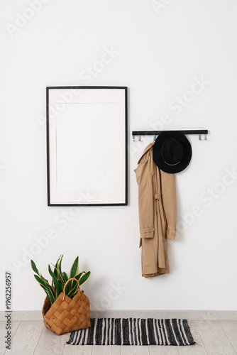Interior of light hallway with stylish hat, coat and blank frame