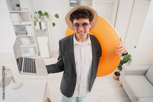 Young businessman with laptop and swim ring waiting for summer vacation in of...