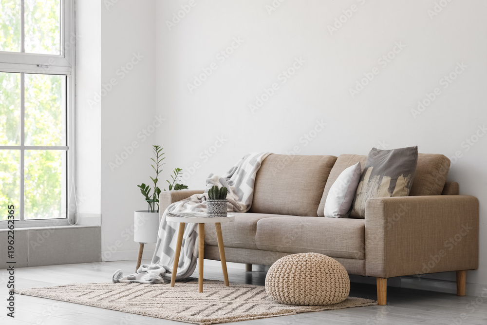 Naklejka premium Interior of light living room with grey sofa, table and pouf