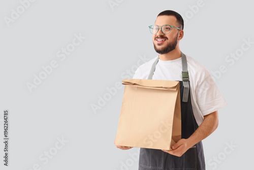 Male worker with paper bag on light background. Food delivery service