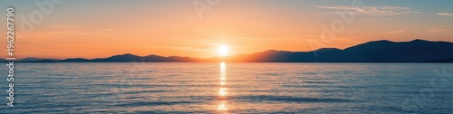 Sun setting behind distant mountains, reflecting orange light on the calm ocean surface. Serene nature scene at twilight