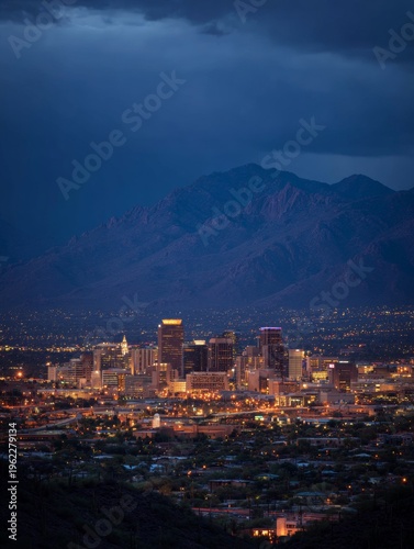 Dark blue night sky over lit cityscape with mountains and valley in background.
