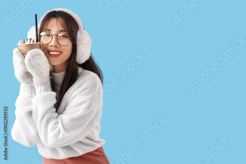 Young Asian woman with cup of hot chocolate on blue background