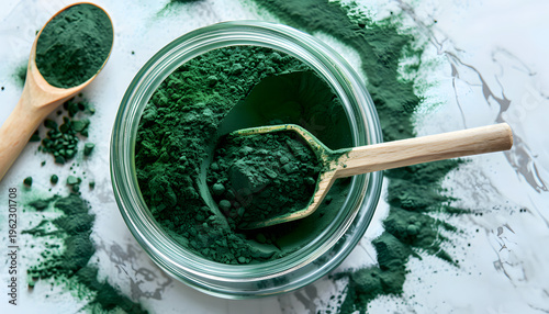 Spirulina powder in clear jar with wooden scoop, artistic powder arrangement on white marble surface, bright natural light, detailed flat lay, modern clean superfood