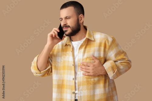 Young man suffering from heart attack and talking with mobile phone on beige ...
