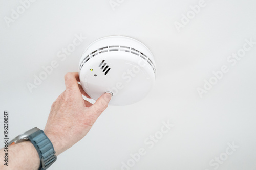 Obraz na plátne Homeowner seen conducting a weekly siren test on a ceiling mounted smoke and carbon monoxide detector located in a hallway