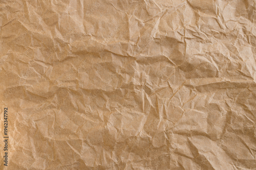 Fototapeta premium Crumpled Brown Kraft Paper Texture Background,Macro,Close-up top view of a wrinkled and crumpled brown kraft paper sheet. This textured background features organic creases, folds, and shadows, perfect