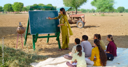 Fotografi Indian young adult gen z female lady talk speak teach to villager child day under tree rural area