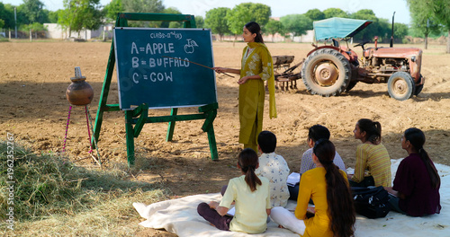 Obraz na plátně Indian young adult gen z female lady talk speak teach to villager child day under tree rural area