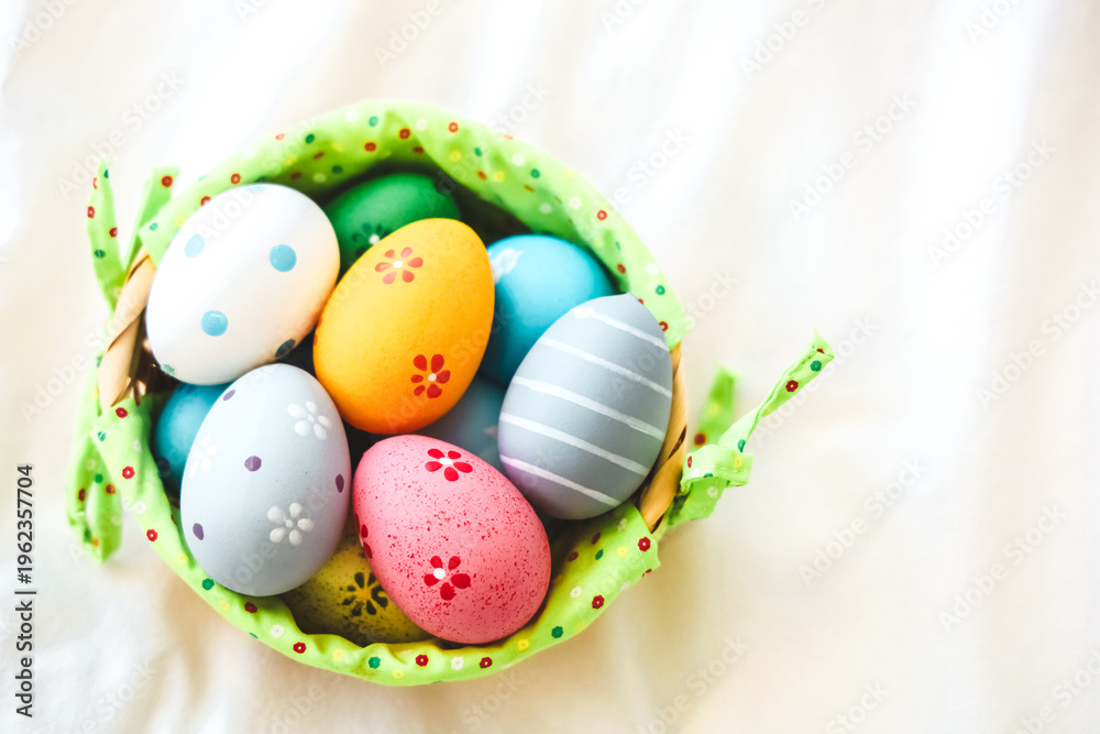 Fototapeta premium Colorful eggs in a small basket on a light background during spring celebration of Easter holidays