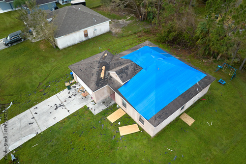 Tablou pe pânză Hurricane Ian damaged house rooftop covered with protective plastic tarp against rain water leaking until replacement of asphalt shingles