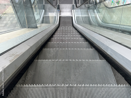 POV modern escalator stairs in urban building interior showing symmetry lines and strong perspective. in shopping center metal steps and glass railing create clean architectural detail in a modern