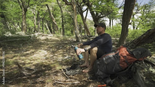 Hiker sitting in a forest drinking water from a bottle in nature