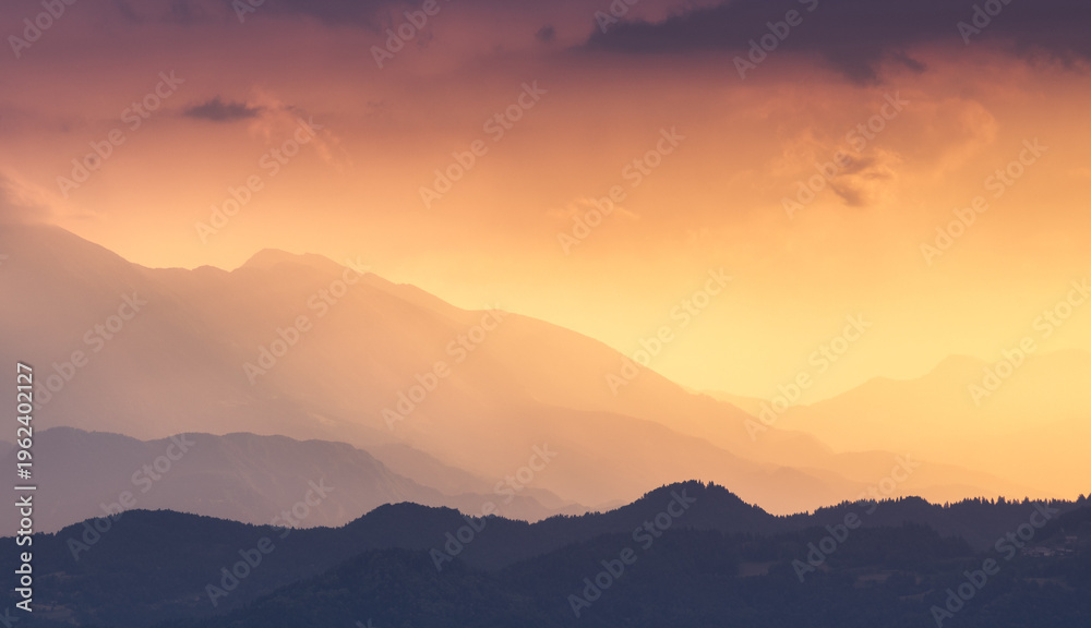 Fototapeta premium Silhouettes of Alpine mountains at colorful sunset in summer in Slovenia. Landscape with mountain ridges in fog, golden sunlight and clouds in the evening. Alps. Nature. Hills in sunlight. Scenery