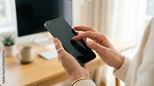 Hands using smartphone near computer monitor on desk