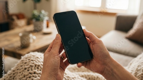 Hands holding smartphone with blank screen in living room