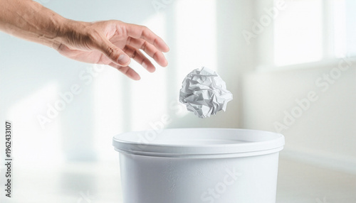 Hand throwing crumpled paper ball into a white trash can in bright room　明るい部屋で白いゴミ箱に丸めた紙屑を投げ入れる手　コピースペース付き