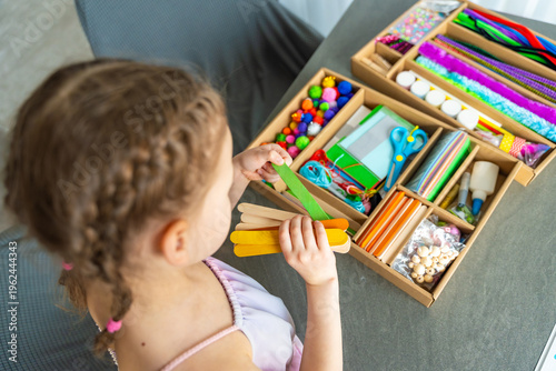 Little girl choosing colorful craft materials from box while preparing creative activity at table. Kids creativity development decision making and learning through play concept.
