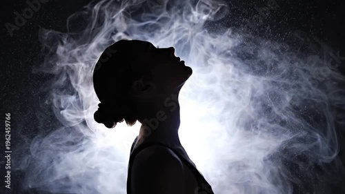 Silhouette of woman standing in thick smoke against dark background