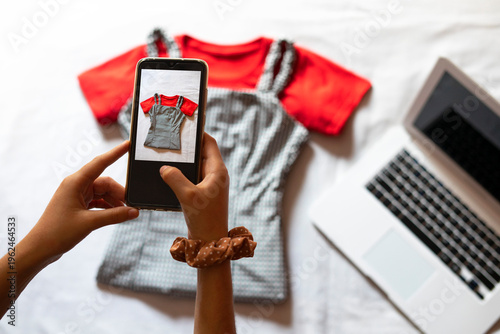Woman taking a photo with the phone of clothing to sell online. Selling clothes online. Second-hand clothes.