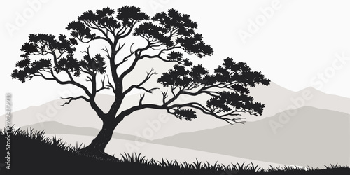 A solitary tree stands tall on a hill with a scenic mountain backdrop at sunset.