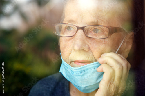 Portrait of an elderly woman in a window after quarantine with her mask removed. An old woman in a window with her mask down, after the pandemic.